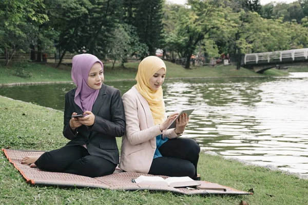 Potret wanita muda campuran yang menyenangkan duduk di rumput di taman musim panas yang hijau dan berdiskusi — Stok Foto