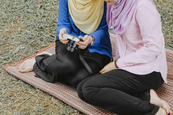 잔디에 앉아 hijab와 젊은 무슬림 컴팩트 카메라에 그들의 사진 미리 보기. — 스톡 사진