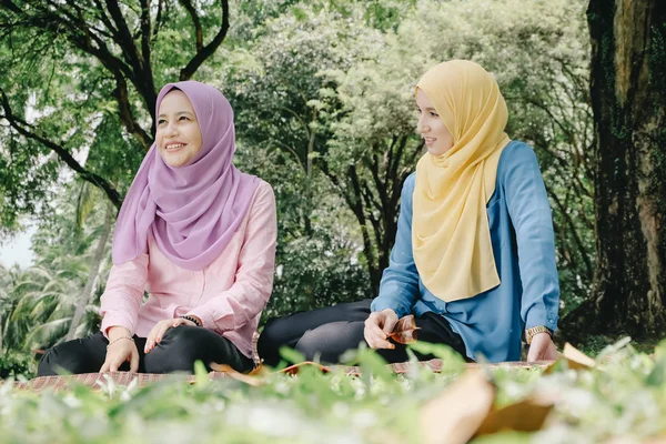 Friendship and happiness concept. portrait of smile young muslimah sitting on grass at city park — Stock Photo, Image