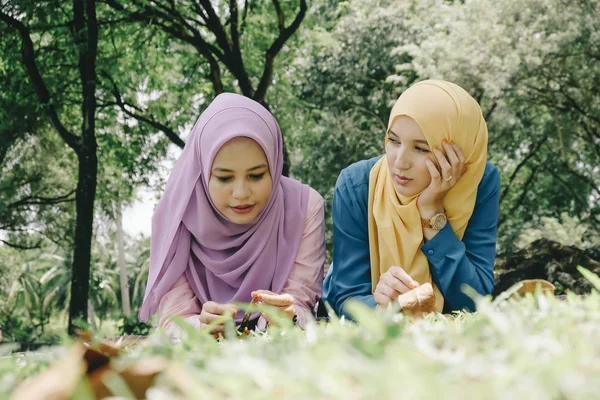Concepto de amistad y felicidad. retrato de sonrisa joven musulmán sentado en la hierba en el parque de la ciudad — Foto de Stock