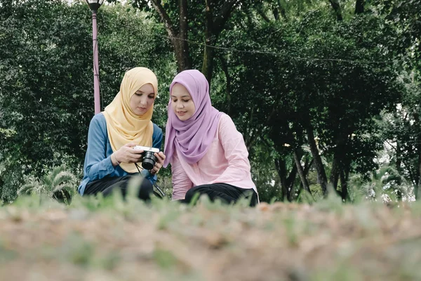 Женщин, наслаждающихся природой, сидящих на зеленой траве в парке и просматривающих свои фотографии через компактную камеру — стоковое фото