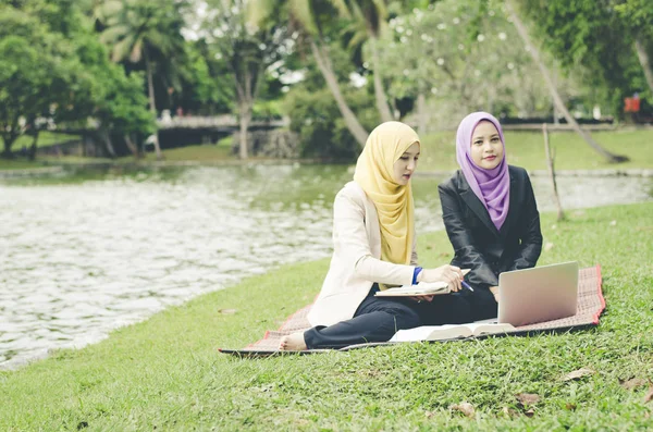 Potret wanita muda campuran yang menyenangkan duduk di rumput di taman musim panas yang hijau dan berdiskusi — Stok Foto