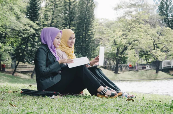 Potret wanita muda campuran yang menyenangkan duduk di rumput di taman musim panas yang hijau dan berdiskusi — Stok Foto