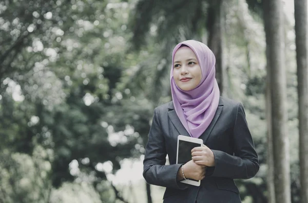 Sonriente joven profesional musulmana mujer de negocios sosteniendo una tableta en el parque —  Fotos de Stock