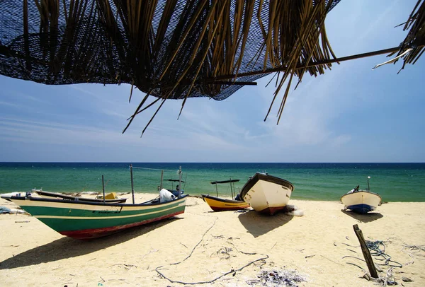 Paisaje bajo cabaña de bambú, barco pescador tradicional varado en la playa de arena desierta bajo día soleado brillante . — Foto de Stock