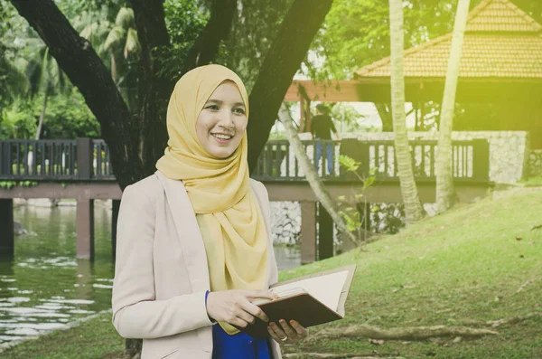 教育理念, 微笑面对年轻的 muslimah 女子站在公园里手持笔记本. 文本的负空格 — 图库照片