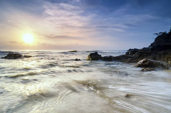 Ειδυλλιακό τροπικό τοπίο κατά τη διάρκεια του ηλιοβασιλέματος, απαλό κύμα χτύπημα βράχο στην ακτή — Φωτογραφία Αρχείου