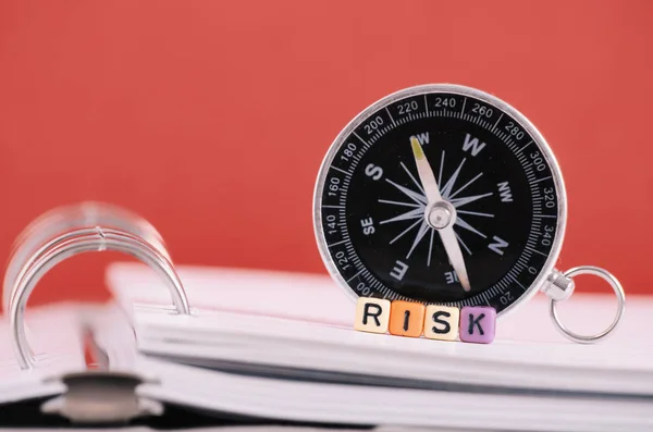 Concepto de gestión de riesgos.Palabra de riesgo cubo en libro sobre brújula y fondo rojo — Foto de Stock