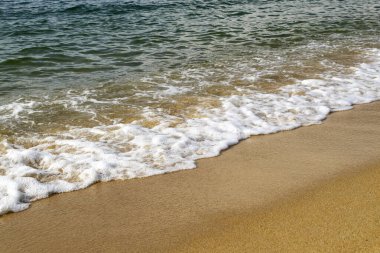 Yumuşak dalgalar güneşli bir günde kumlu sahile vurur