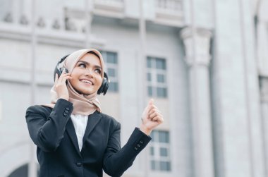 Mutlu ve neşeli bir ifade, siyah takım elbiseli güzel bir kadın ve müzik dinlerken gülümseyen bir tesettür.