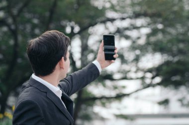 Siyah takım elbiseli genç bir iş adamının portresi ortaklarla video görüşmesi veya selfie çekmek için cep telefonu kullanıyor.