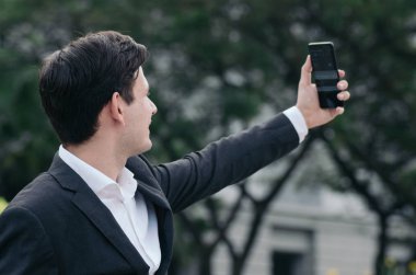 Siyah takım elbiseli genç bir iş adamının portresi ortaklarla video görüşmesi veya selfie çekmek için cep telefonu kullanıyor.