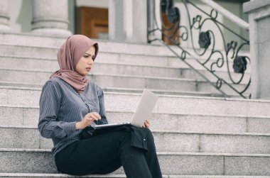 Mutsuz yüz ifadesi, merdivenlerde oturan genç iş kadını ve dizüstü bilgisayarına bakması. 