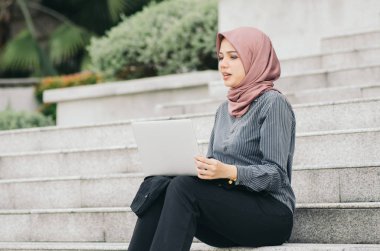 Başarılı ve kendinden emin ifade, yıldızların üzerinde oturan ve dizüstü bilgisayarıyla çalışan genç yönetici kadın.