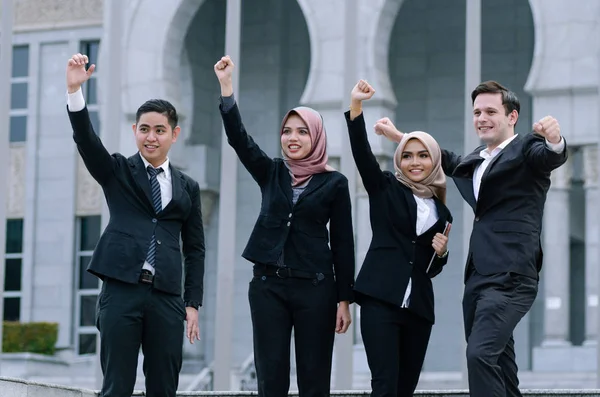 Group of young executive people in formalwear, arms raised to celebrate their success