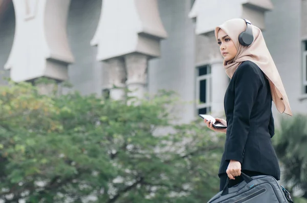 Retrato de una hermosa mujer en traje negro y hijab sonriendo escuchando música —  Fotos de Stock