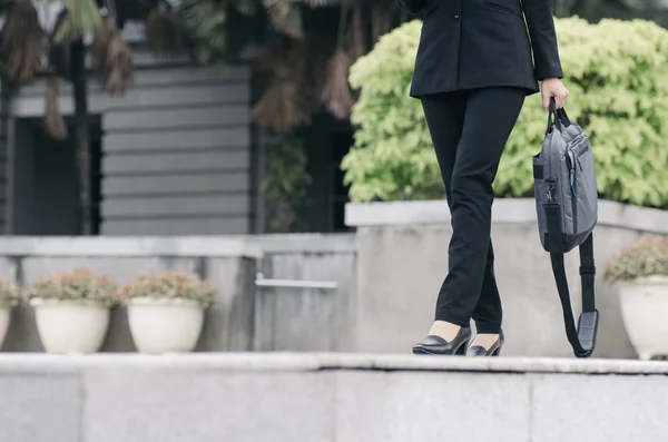 unidentified young executive businesswoman in black suit walking with sling bag