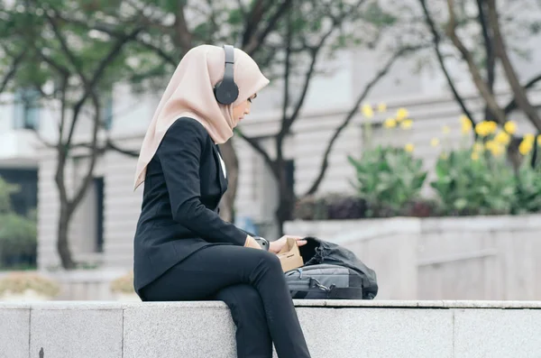 Retrato de una hermosa mujer en traje negro y hijab sonriendo escuchando música —  Fotos de Stock