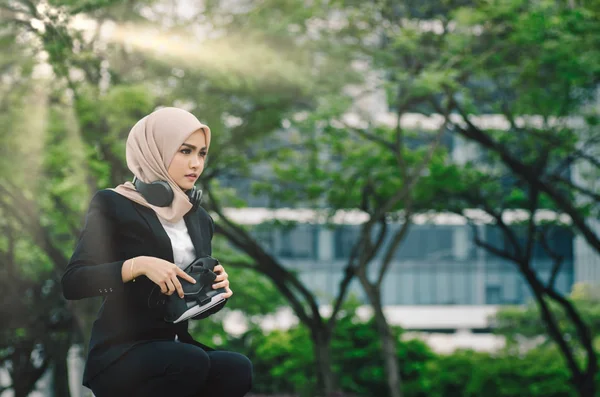 Retrato de una hermosa mujer en traje negro y hijab sonriendo escuchando música — Foto de Stock