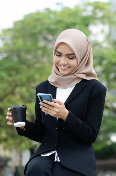 Retrato de mujeres de negocios jóvenes en traje negro y hijab usando teléfono inteligente y sosteniendo la taza de café —  Fotos de Stock