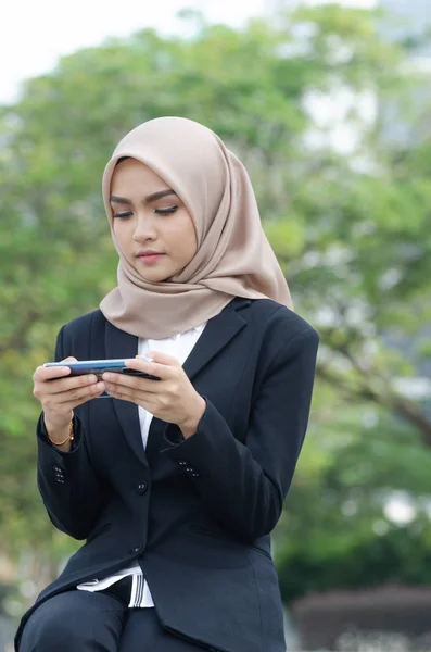 Retrato de una joven mujer de negocios sentada afuera y enviando mensajes de texto a alguien usando su teléfono —  Fotos de Stock