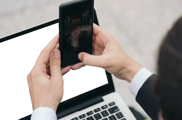 Неопознанный бизнесмен в элегантном костюме, сидит с ноутбуком и фотографируется с помощью мобильного телефона — стоковое фото