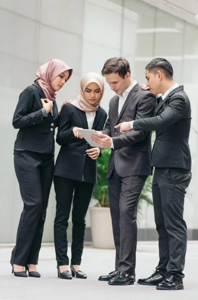 Group of young executive people in formalwear holding tablet and discussing something.