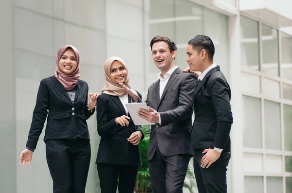 Group of young executive people in formalwear holding tablet and discussing something with happy face expression