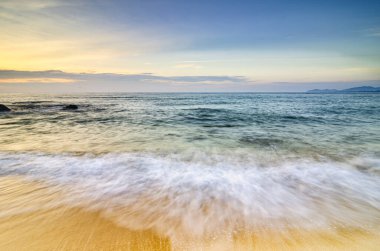 Sahilde güzel bir sabah arkaplanı. Kıyı şeridine vuran ve bulutlu gökyüzüne vuran yumuşak bir dalga
