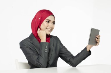 İletişim konsepti, tesettürlü genç bir kadın gülümseyen yüzüyle oturuyor, tabletine bak.