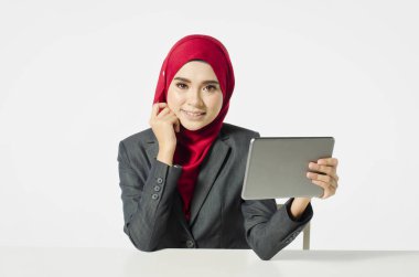 İletişim konsepti, tesettürlü genç bir kadın gülümseyen yüzüyle oturuyor, tabletine bak.