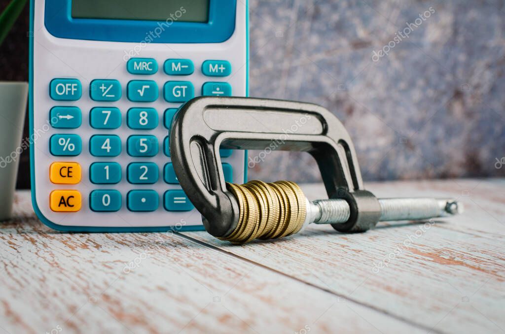 Financial crisis concept, calculator and stacking coin squeezing in a G-clamp on wooden desk
