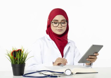 Gülen surat tesettürlü genç doktor beyaz arka planda ofisteki tabletini okudu.