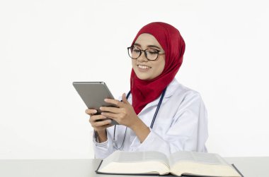 Gülen surat tesettürlü genç doktor beyaz arka planda ofisteki tabletini okudu.