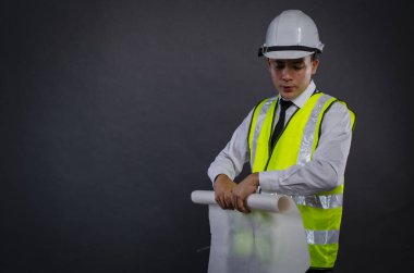 Genç mimar ya da mühendis ayakta ve koyu arkaplan üzerinde mavi baskı kağıdı tutuyor