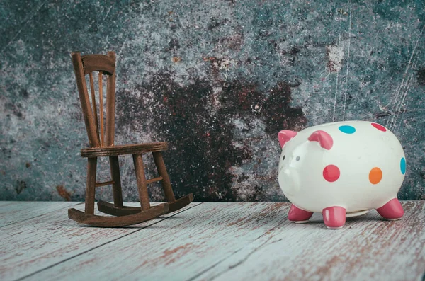 Saving for retirement concept, piggy bank and wooden chair on desk over aged wall background