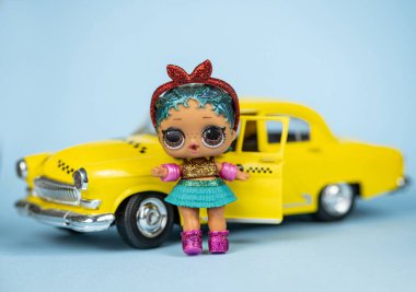 Bir LOL. Sarı arabanın yanında mavi arka planda sürpriz bebek.