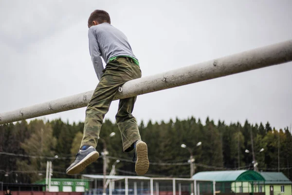 The child is sitting on the pipe. The boy climbed the gate