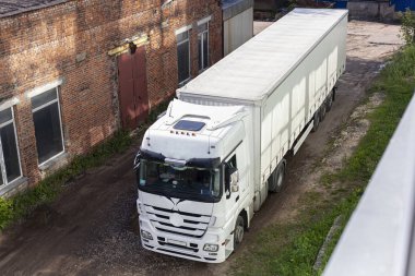 Kamyon depoya vardı. Nakliye aracının üst görüntüsü. Büyük araç gereçler. Evler arasında geçişi daralt.