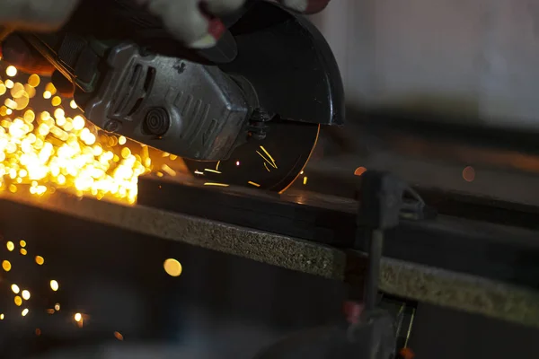 Metal cutting. Grinding steel. Work as a grinder. Sparks from friction. Men's work. Creating a design. The project in the workshop. Iron processing. Hand electric tool.