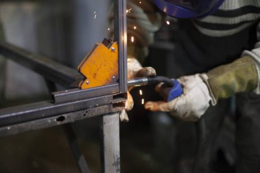 Kaynakçı işte. Kaynakçı metali ısıtır. Atölyedeki dersler. Çelik işleme. Mavi kaynak maskeli bir kaynakçı. Yüksek erime noktası. Sıkı çalışan bir adam..