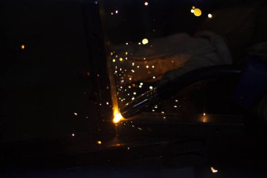 Metal kıvılcımlar. Sıcak çelikten ateş. Acil bir iş. Öğütücüyle çalış. Demir ışıklar lehimleniyor. Koyu bir arka planda, sıcak talaş yağmuruna karşı ateş ediyorlar. Güçlü sıcaklık. Atölye çalışması. Yapı için parçalar üretiliyor.