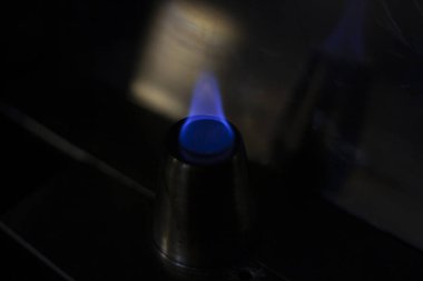 Alkol, alkollü içecekler için yığınla yakar. Metal bir bardağın etrafında alev dilleri. Ateşin dokusu. Siyah arka planda sarı ateş. Barda yangın çıktı. Alkolü ateşe verme geleneği..