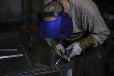 Kaynakçı işte. Kaynakçı metali ısıtır. Atölyedeki dersler. Çelik işleme. Mavi kaynak maskeli bir kaynakçı. Yüksek erime noktası. Sıkı çalışan bir adam..