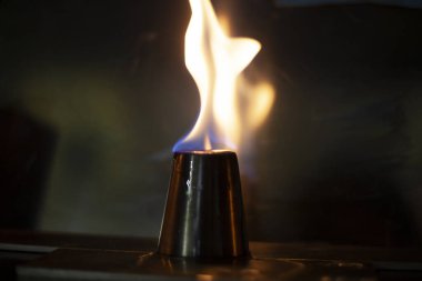 Alkol, alkollü içecekler için yığınla yakar. Metal bir bardağın etrafında alev dilleri. Ateşin dokusu. Siyah arka planda sarı ateş. Barda yangın çıktı. Alkolü ateşe verme geleneği..