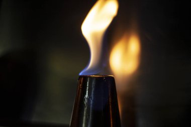 Alkol, alkollü içecekler için yığınla yakar. Metal bir bardağın etrafında alev dilleri. Ateşin dokusu. Siyah arka planda sarı ateş. Barda yangın çıktı. Alkolü ateşe verme geleneği..