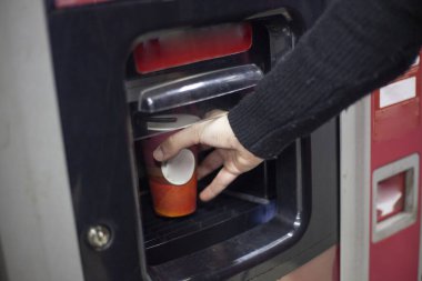 Otomattan sıcak kahve. Bir el, otomatik bir cihazdan elde edilen bir içecekle sıcak bir fincana uzanır. Alışveriş merkezinde kahve. Bir kız, cihazın özel bir bölümünden bir içki alır..