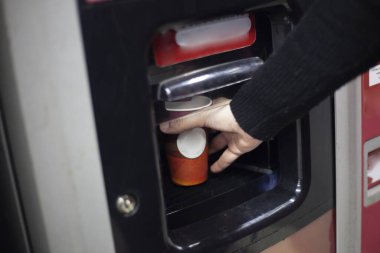 Otomattan sıcak kahve. Bir el, otomatik bir cihazdan elde edilen bir içecekle sıcak bir fincana uzanır. Alışveriş merkezinde kahve. Bir kız, cihazın özel bir bölümünden bir içki alır..