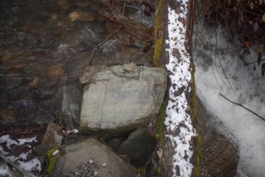 Bir dağ nehri taşların üzerinden akar. Nehir kışın dağlarda. Kayalık bir yamaç boyunca akan bir su. Buzuldan gelen temiz su kayalık bir taban boyunca akar..