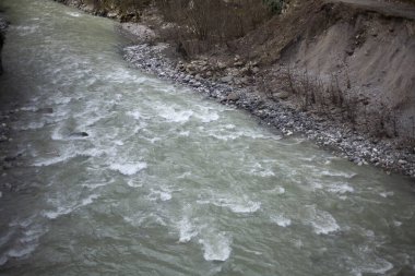 Bir dağ nehri taşların üzerinden akar. Suyun hızlı akışı. Doğal arka plan. Su kütlesinin kayalık tabanı boyunca hareket hızı. Küçük bir nehrin dalgalarının dokusu.